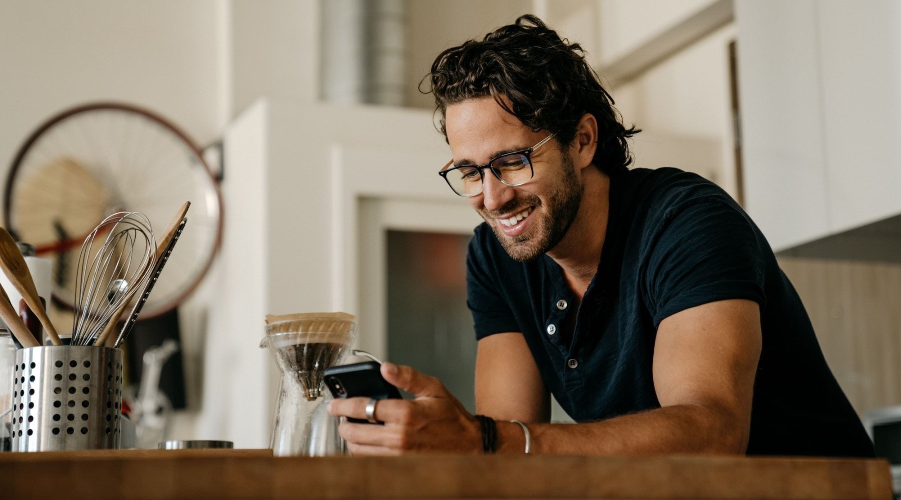 a person smiling looking at a phone making coffee in a kitchen