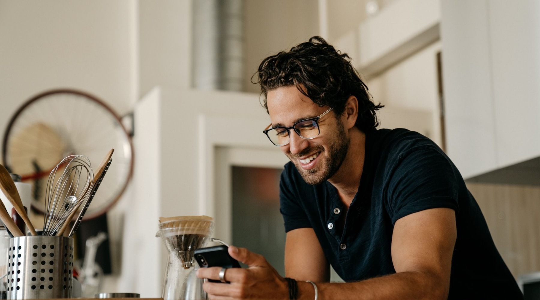 a person smiling looking at a phone making coffee in a kitchen